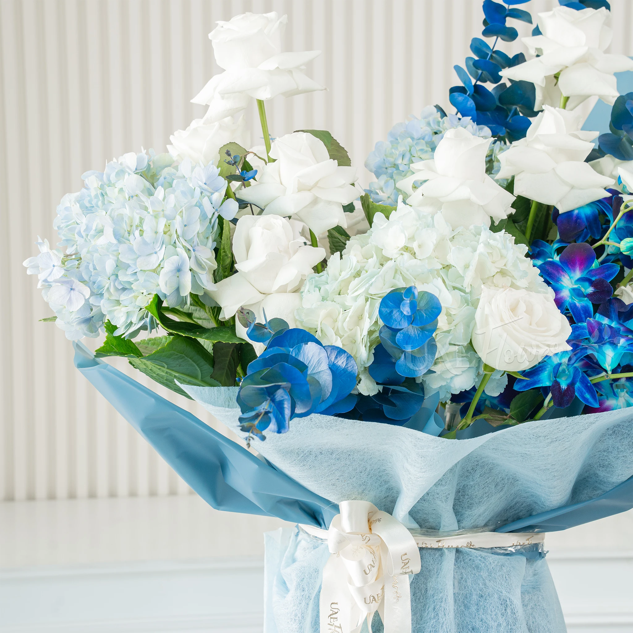 Bouquet of blue hydrangeas, white roses, and blue orchids wrapped in blue paper, a serene floral arrangement for special celebrations.