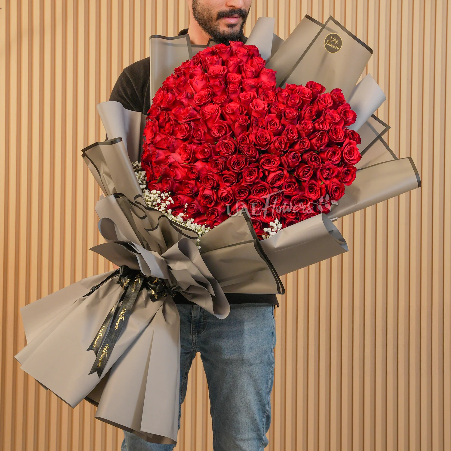 Heart-shaped bouquet of 100 red roses with baby’s breath fillers wrapped in elegant black paper and ribbon