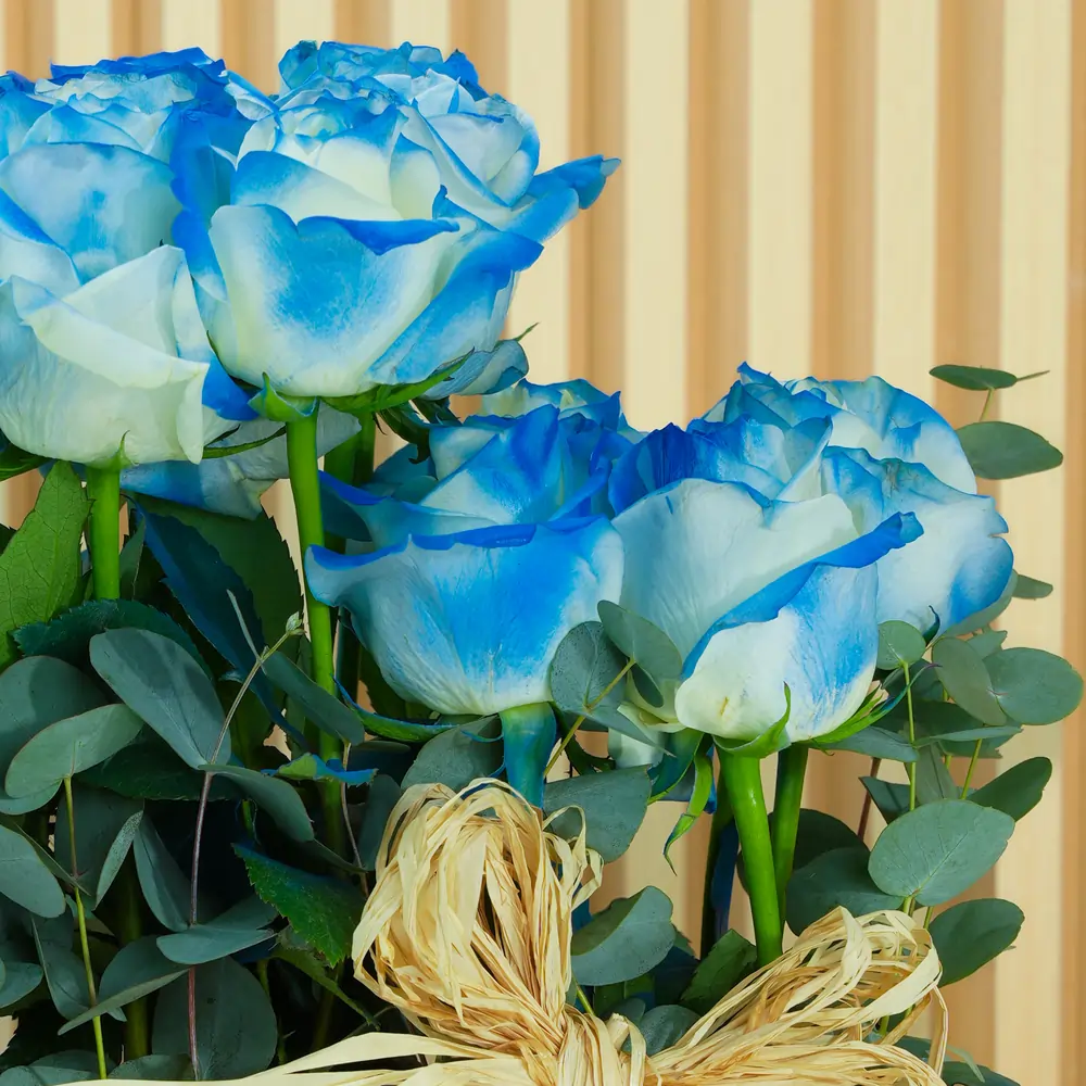 Beautiful blue roses arranged in a rustic woven basket with greenery, tied with a natural raffia bow, perfect for gifting or home decor.