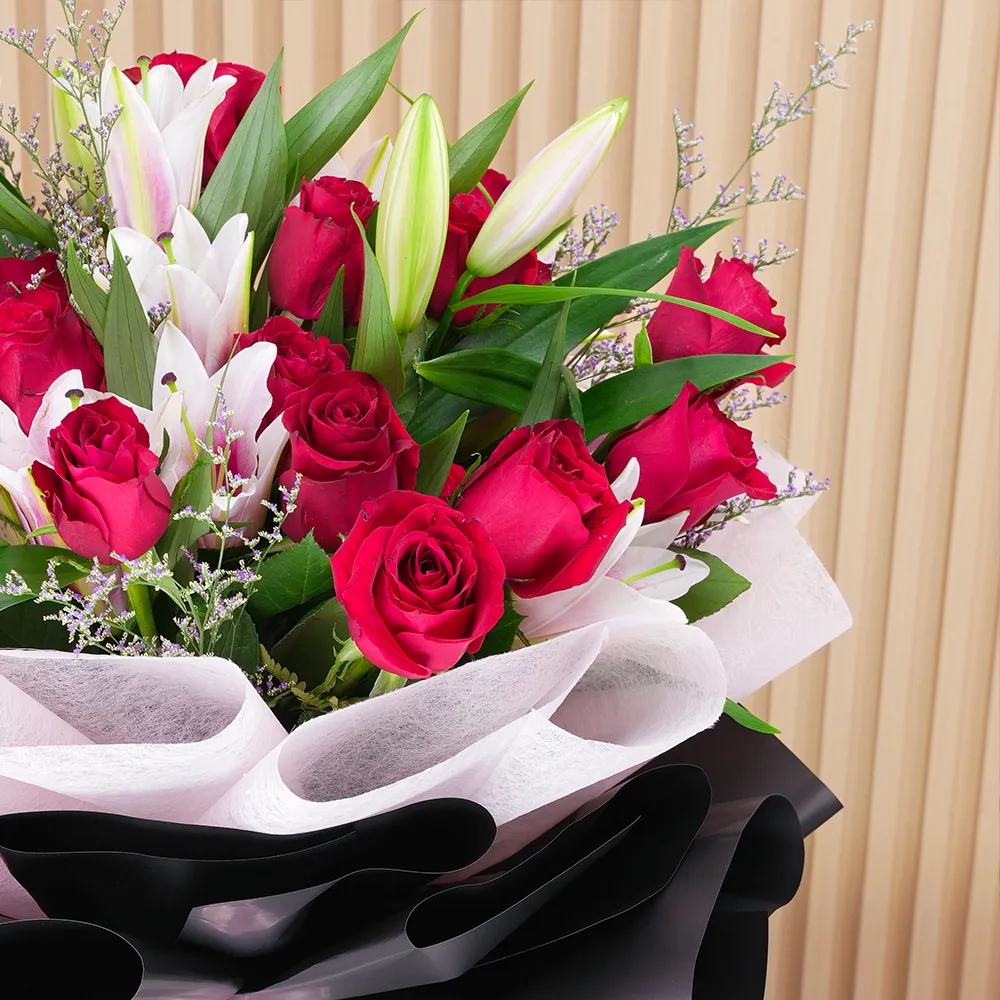 A bouquet of 4 pink lilies & 10 red roses in pink wrapping paper tied with a pink ribbon