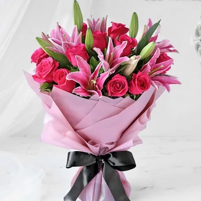 A bouquet of 12 pink roses and 3 pink lilies with fillers in pink wrapping paper tied with black ribbon