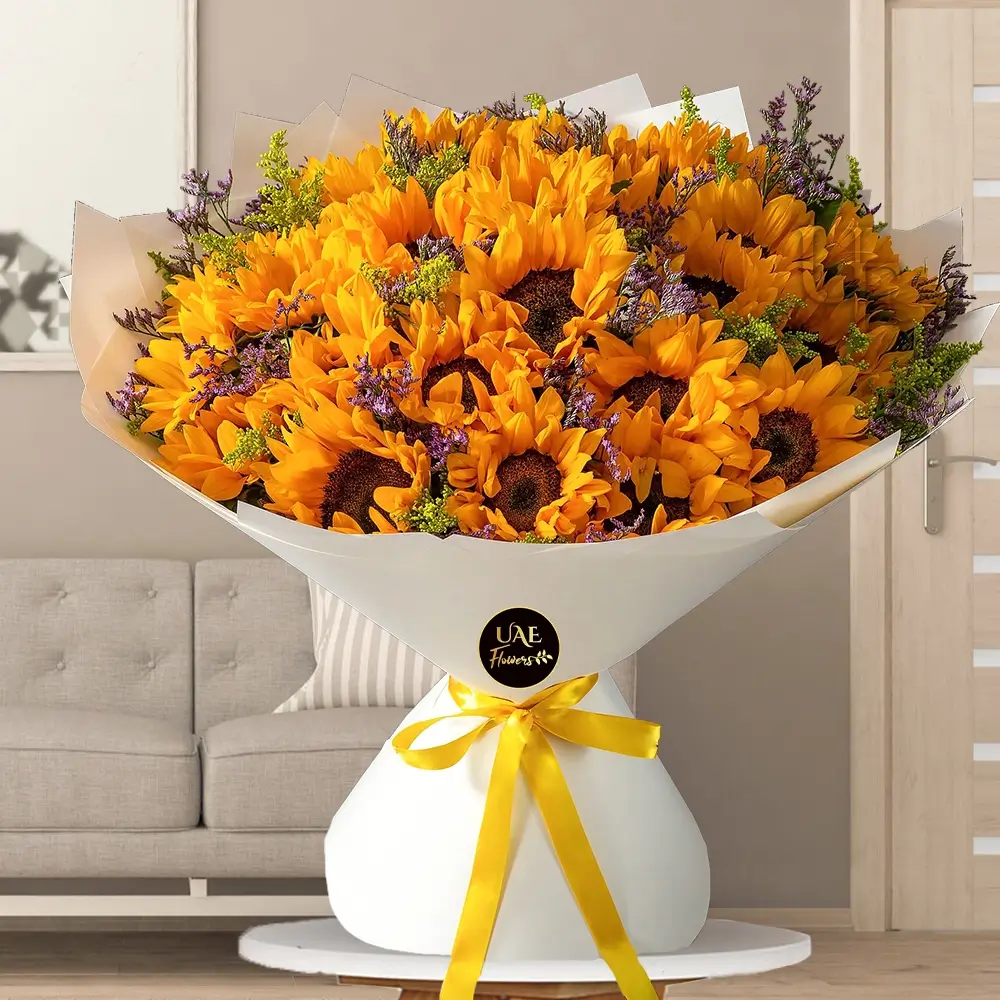 A bouquet of 25 sunflowers with greens in white wrapping paper tied with yellow ribbon