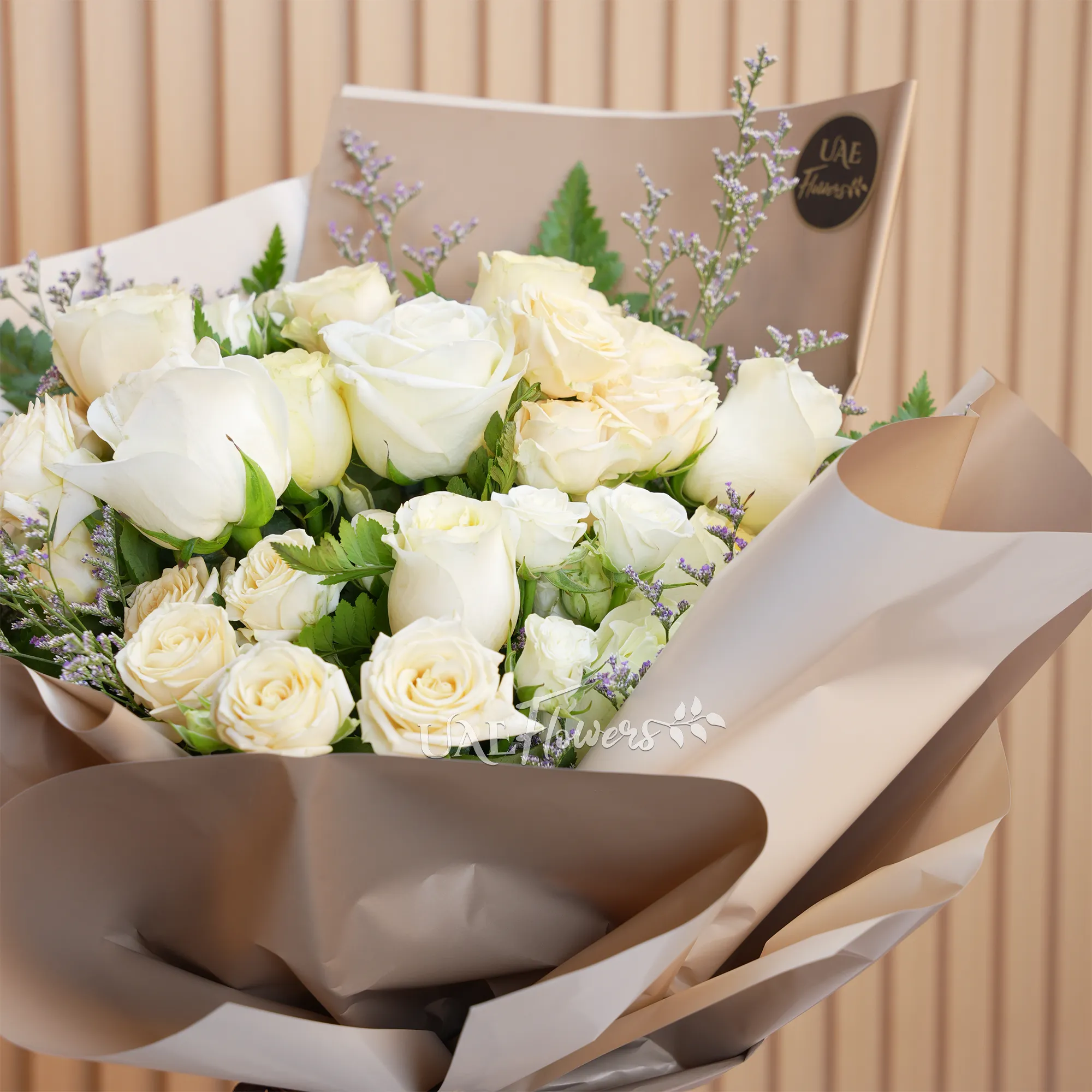 Bouquet of 8 white and peach roses with 2 peach spray roses and green fillers, wrapped in paper and tied with ribbons.
