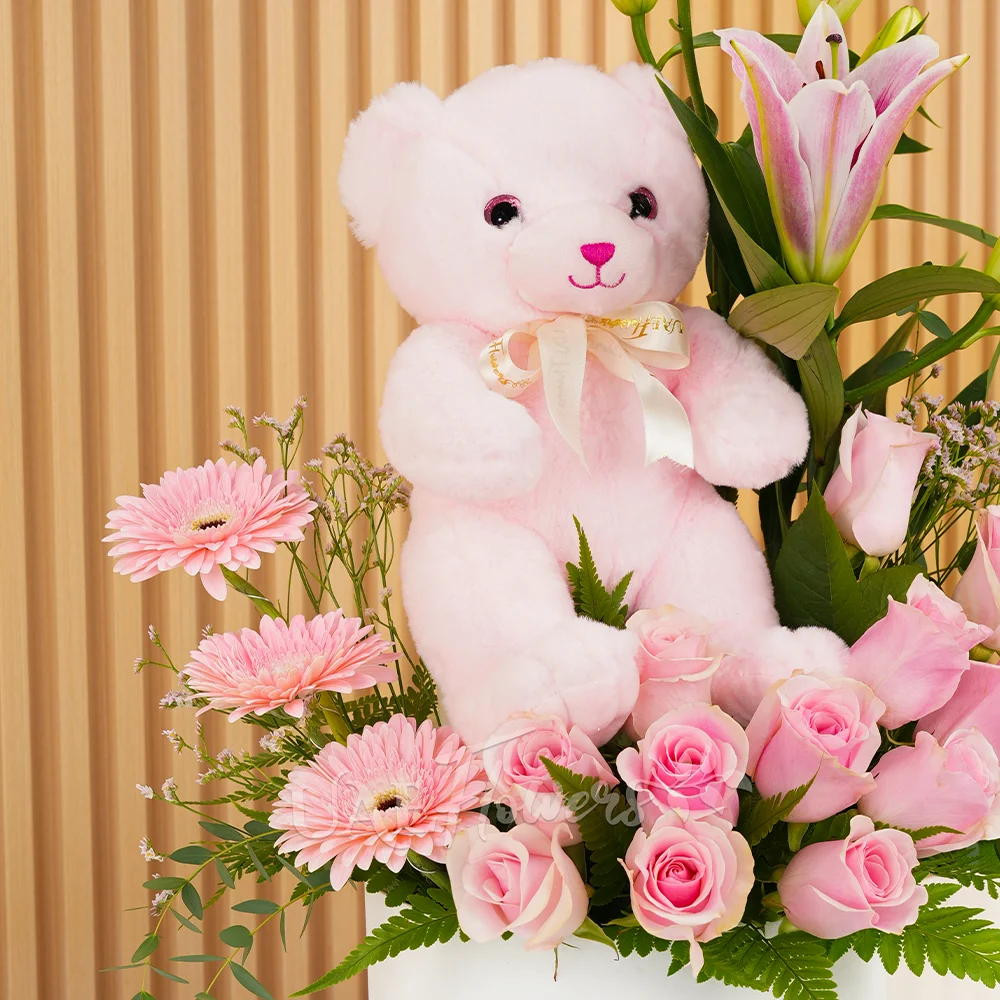 pink lily, pink gerberas, and pink roses in a round white box with a small pink teddy bear
