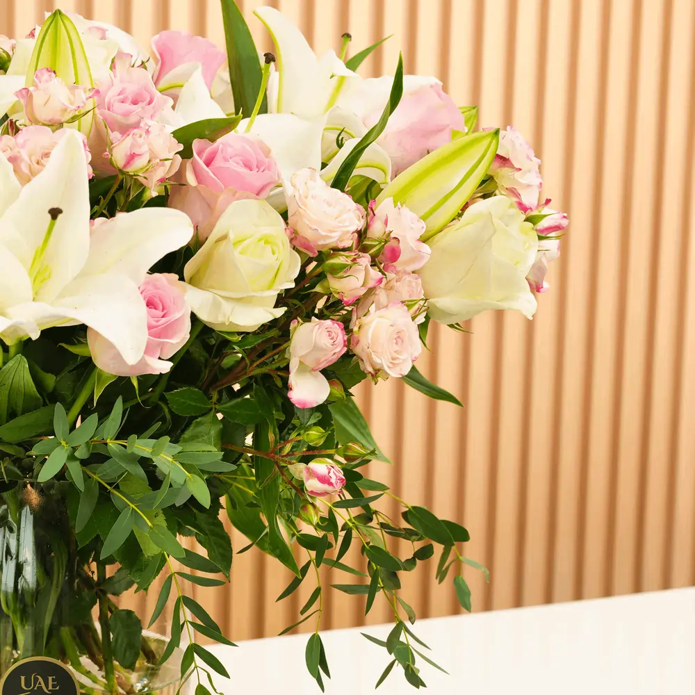 Glass vase with white lilies, pink and white roses, pink spray roses, and green fillers arranged elegantly