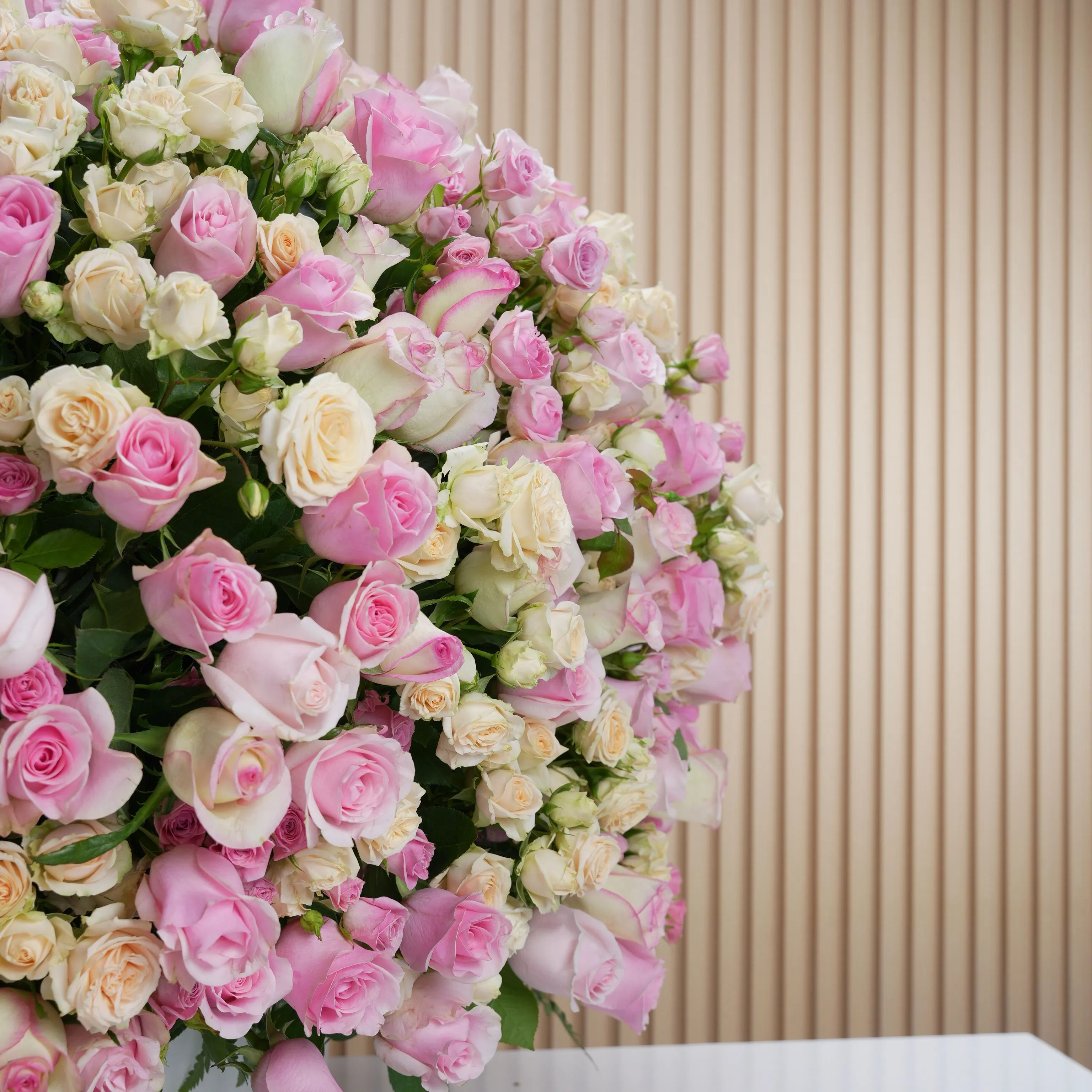 round arrangement of 100 light and dark pink roses and peach spray roses in a round box.
