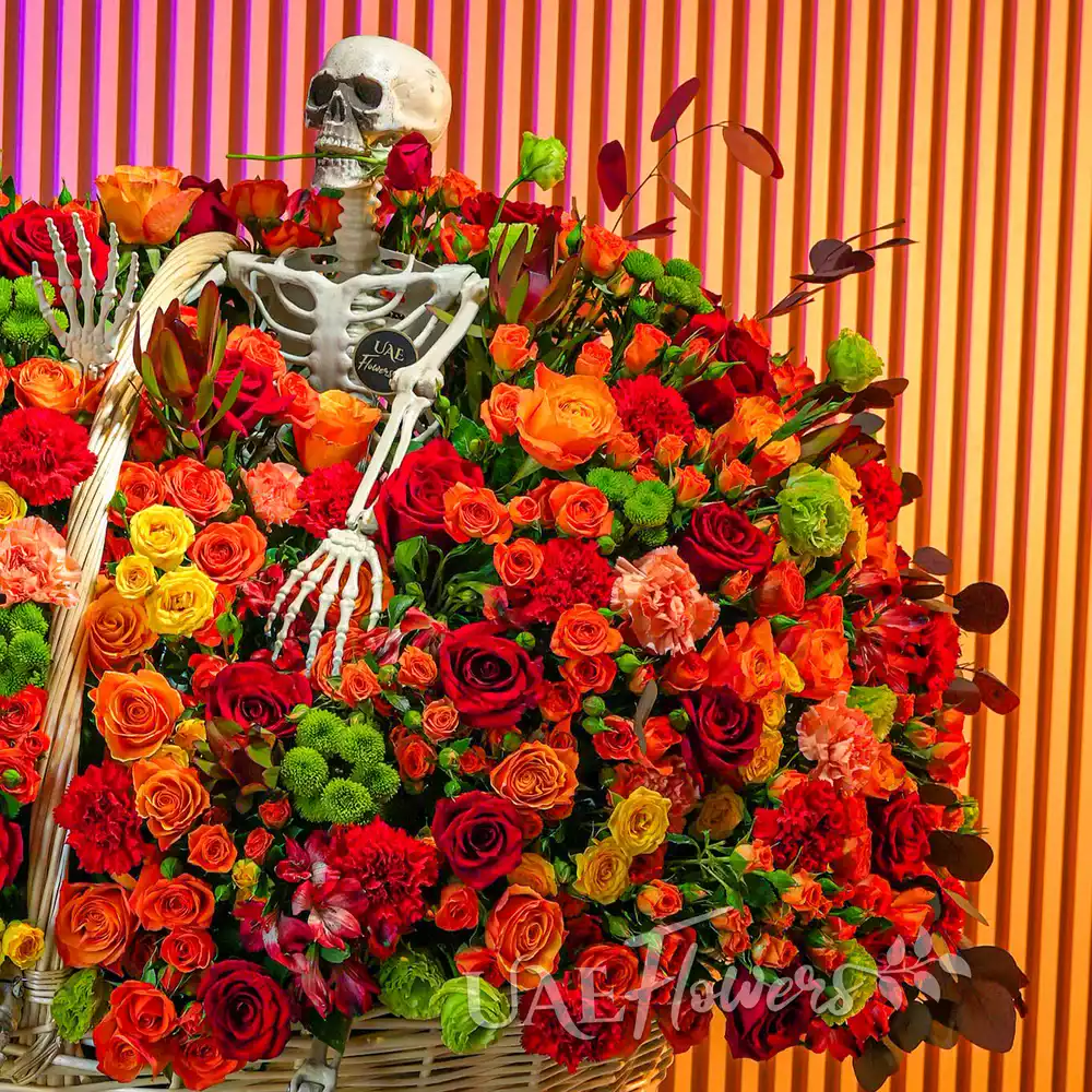 Round basket with orange and yellow spray roses, red roses, carnations, chrysanthemums, and Alstroemeria arranged with ribbons